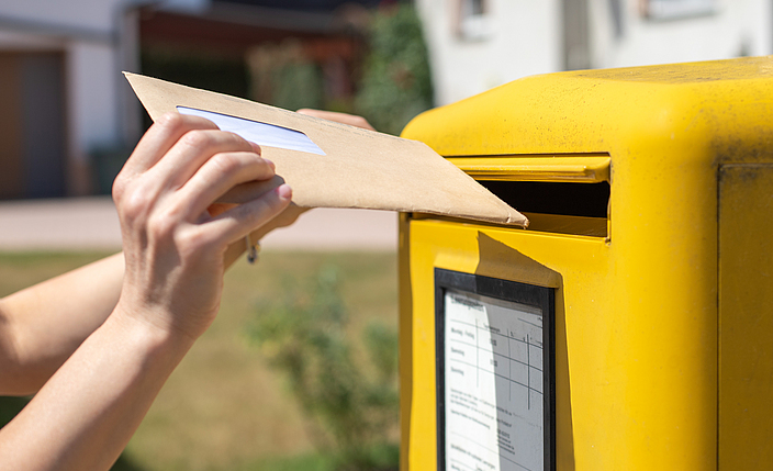 Ein Brief wird in einen Briefkasten geworfen.
