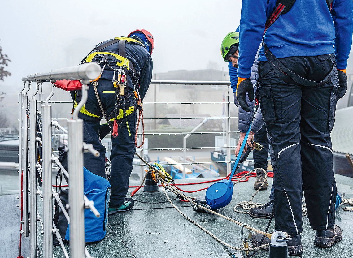 Dachdecker bei der Unterweisung mit Persönlicher Schutzausrüstung gegen Absturz auf einem Flachdach. 