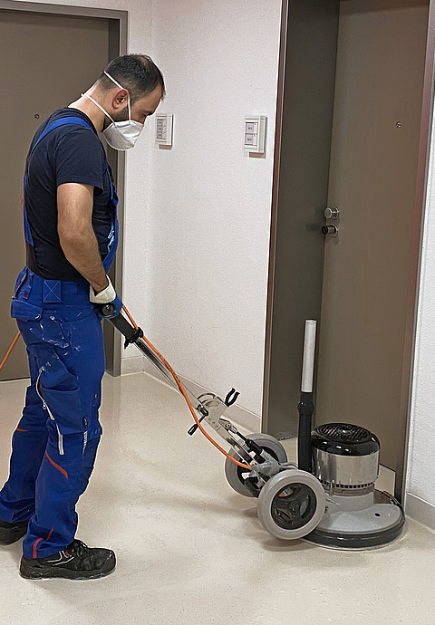 Mann beim Reinigen eines Fußbodens mit einer Reinigungsmaschine.
