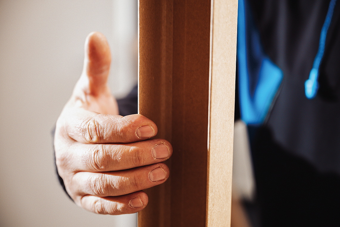 Eine Hand hält ein Trockenbauprofil aus Zellstoff an der Oberkante. 