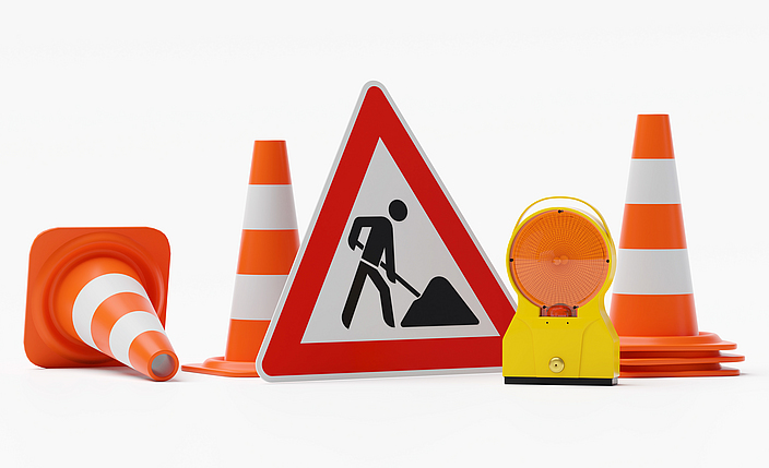 Schild: Warnung Baustelle  mit Baustellenleuchte und mehreren Verkehrshütchen.