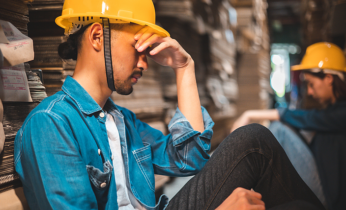 Ein sitzender Bauarbeiter legt seine Hand an die Stirn.
