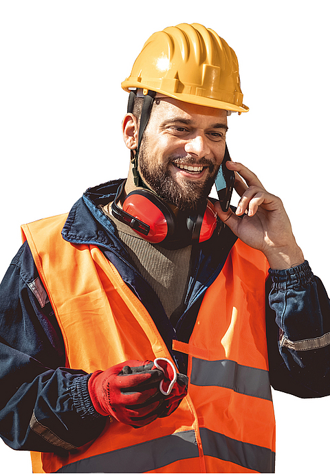 Ein Bauleiter mit Sicherheitsweste und Helm telefoniert auf der Baustelle.
    
