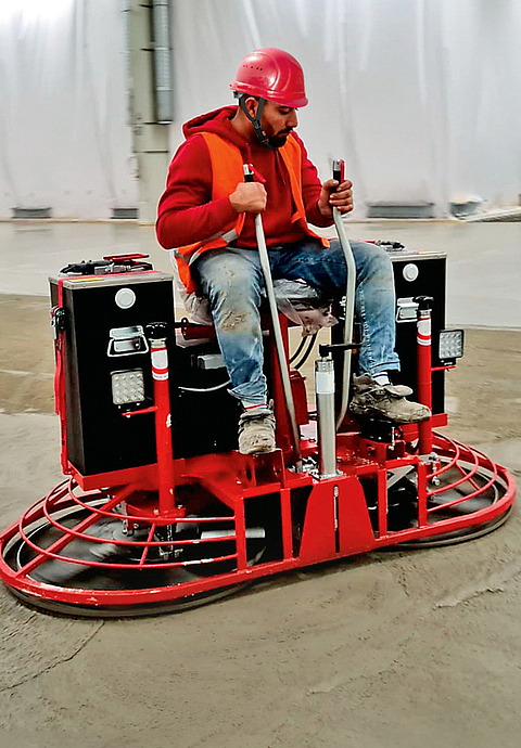 Ein Mann mit Schutzhelm und Warnweste bedient einen akkubetriebenen Doppelglätter. 