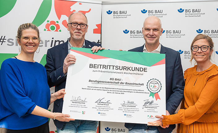 Janina Führ (BG BAU, Referatsleiterin), Ralf Hövelmann (Netzwerk #sicherimDienst), Michael Kirsch (Hauptgeschäftsführer der BG BAU), Katia-Julia Rostek (stellv. Hauptgeschäftsführerin der BG BAU) halten die unterzeichnete Beitrittsurkunde. 