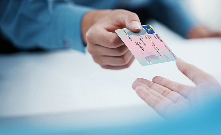 Zwei Hände übergeben einen Führerschein zur Kontrolle.