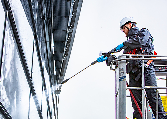 Glasreiniger säubert ein Fenster mit einem Hochdruckreiniger von einer Hubarbeitsbühne. 