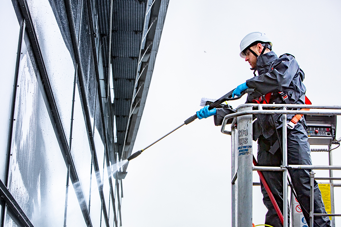 Glasreiniger säubert ein Fenster mit einem Hochdruckreiniger von einer Hubarbeitsbühne. 