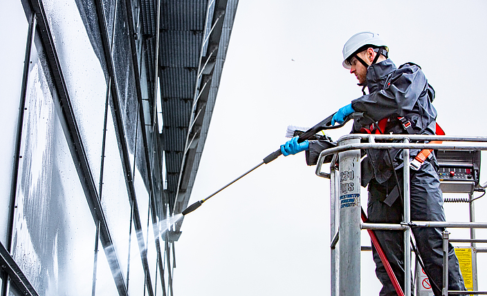 Glasreiniger säubert ein Fenster mit einem Hochdruckreiniger von einer Hubarbeitsbühne. 