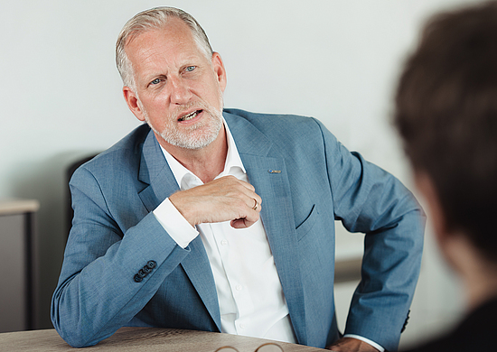 Björn Kass, Präventionsleiter der BG BAU, im Dialog mit einem Gesprächspartner, der mit Unschärfe von hinten abgebildet ist. 
