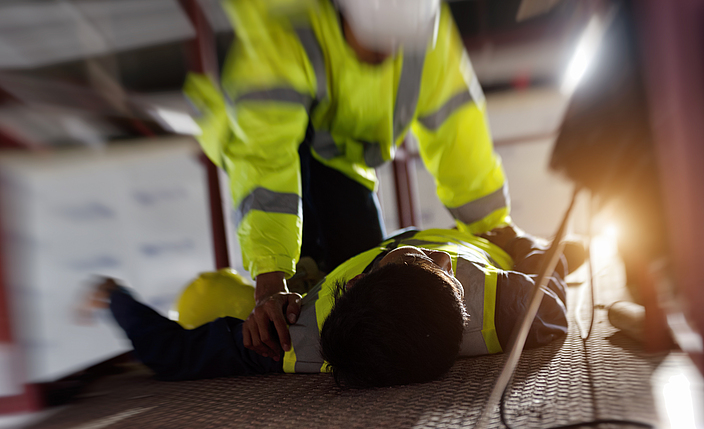 Ein Bauarbeiter leistet einem anderen Bauarbeiter bei einem Arbeitsunfall Erste Hilfe.