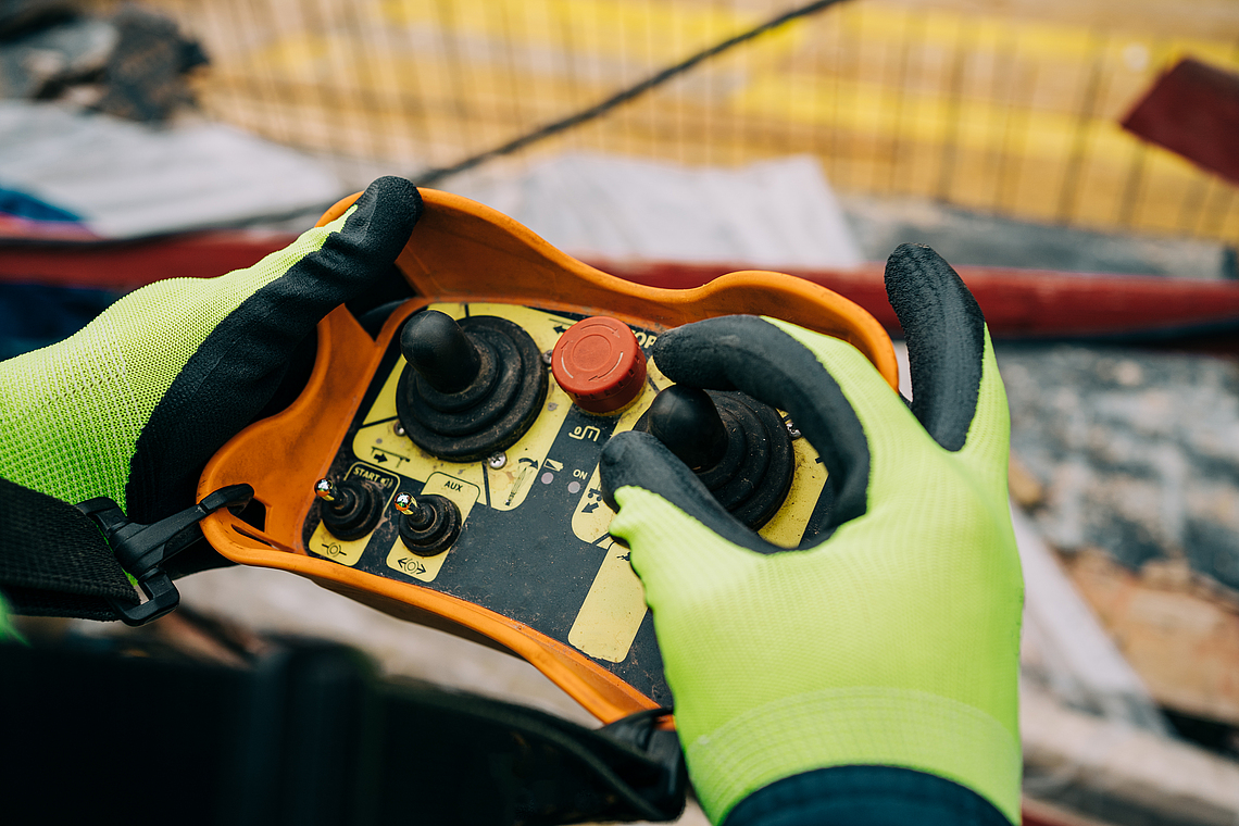 Zwei Hände mit Handschuhen bedienen eine Fernsteuerung. 