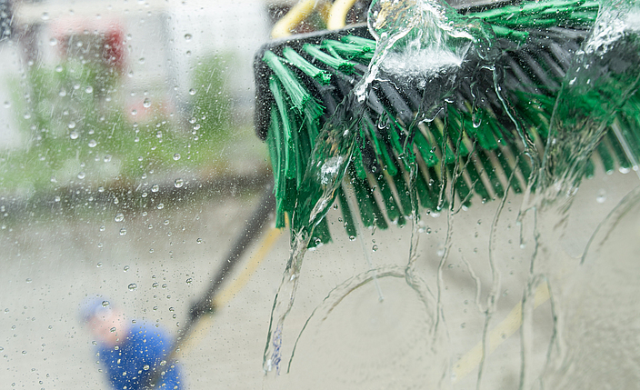 Aufnahme durch ein Fenster zeigt Besen beim Auftrag von entmineralisiertem Wasser bei Fensterreinigung mit Stangensystem.
