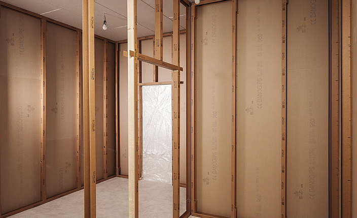 Innenansicht eines Raums im Holzrahmenbau mit freiliegenden Holzständern und Wandplatten im Rohbau. 