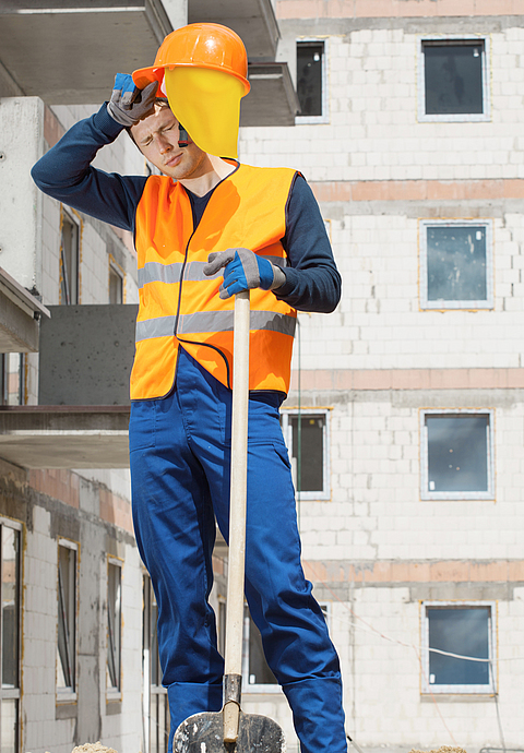 Ein Bauarbeiter arbeitet auf einer Baustelle und ist durch die Sonneneinstrahlung und Hitze erschöpft.
