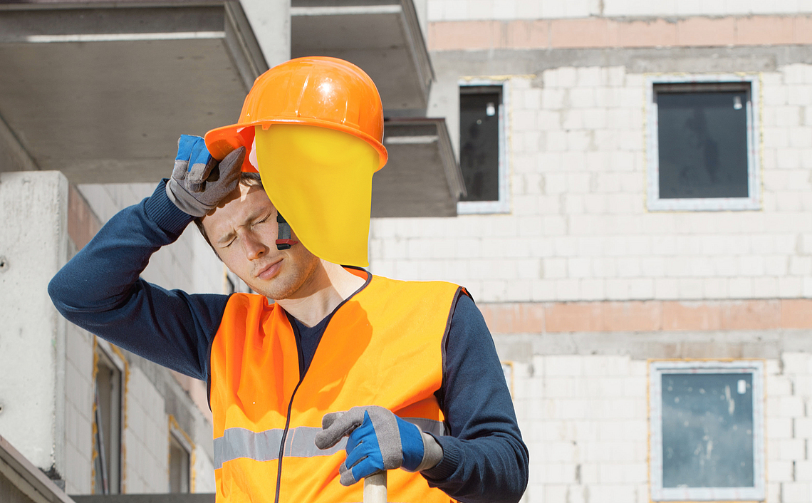 Ein Bauarbeiter arbeitet auf einer Baustelle und ist durch die Sonneneinstrahlung und Hitze erschöpft.
