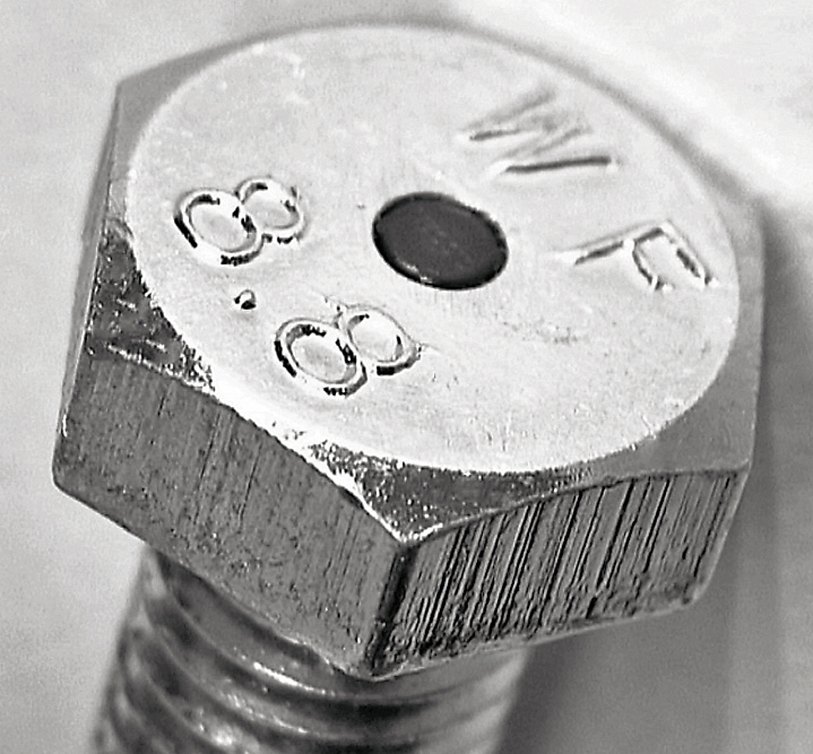 Schwarz-Weiß-Bild eines Schraubenkopfes mit schwarzer, runder Platte in der Mitte.
