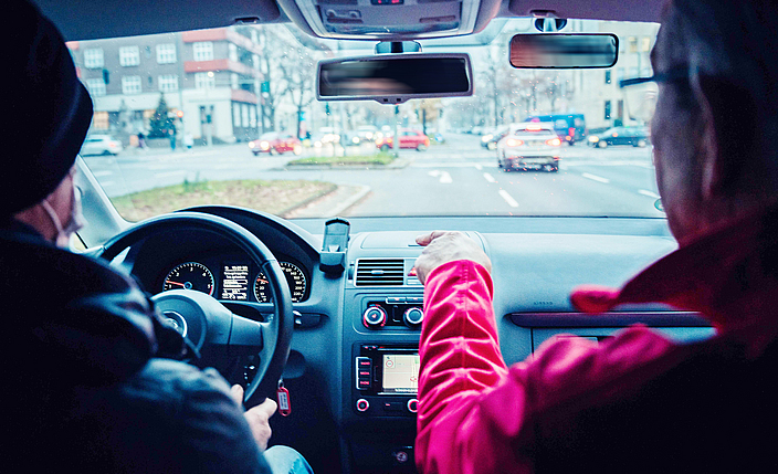 Zwei Personen, Autofahrer und Beifahrer, sitzen in einem Auto und schauen auf den Verkehr.