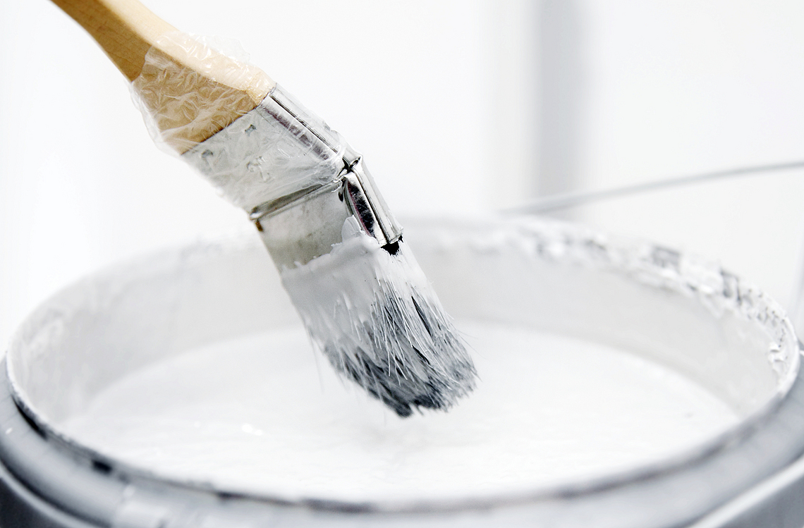Ein Pinsel taucht in weiße Farbe. 