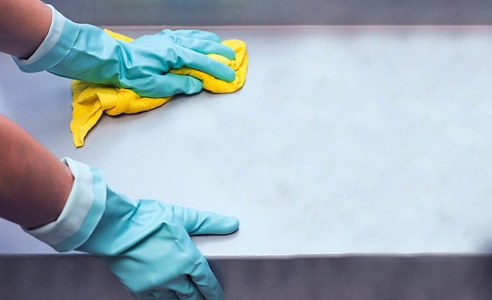 Reinigung einer glatten Oberfläche mit grünen Schutzhandschuhen und einem gelben Lappen.
