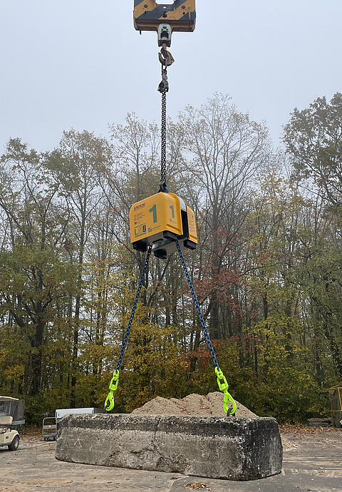 Ein Betonteil hängt an einer orangen Lastausgleichsvorrichtung. 