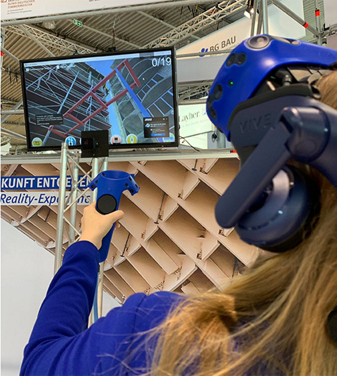 Eine Frau schaut sich mit Hilfe einer VR-Brille eine virtuelle Baustelle auf der Messe Dach + Holz 2020 der BG BAU an. 
