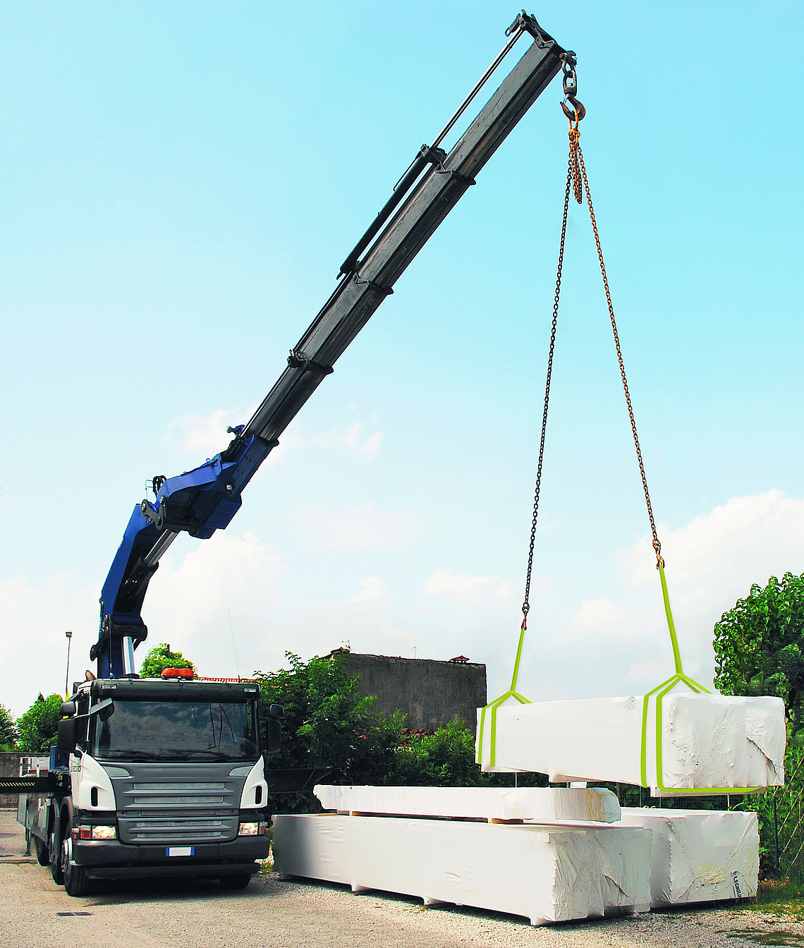 Ein Lkw mit Teleskopkran liefert Holzpakete für ein Holzhaus. Das Holzhaus wird vor Ort montiert. 