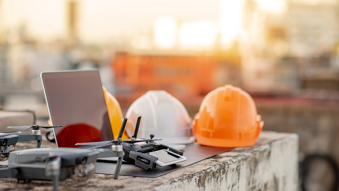 Drohne, Smartphone, Laptop und Schutzhelm auf einer Baustelle. Einsatz von unbemannten Luftfahrzeugen (UAV) für Land- und Baustellenuntersuchungen in Tiefbauprojekten. 