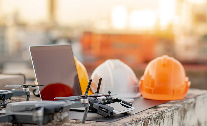 Drohne, Smartphone, Laptop und Schutzhelm auf einer Baustelle. Einsatz von unbemannten Luftfahrzeugen (UAV) für Land- und Baustellenuntersuchungen in Tiefbauprojekten.