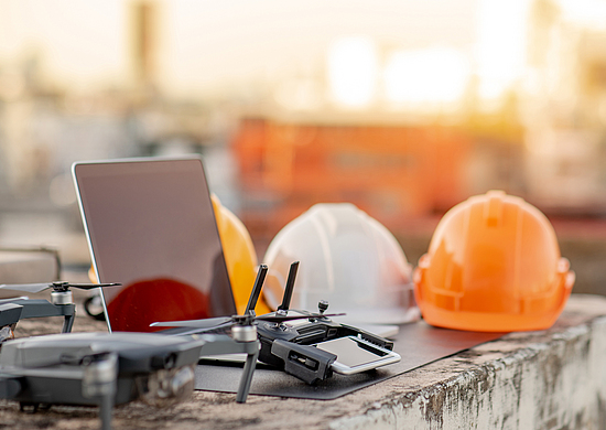 Drohne, Smartphone, Laptop und Schutzhelm auf einer Baustelle. Einsatz von unbemannten Luftfahrzeugen (UAV) für Land- und Baustellenuntersuchungen in Tiefbauprojekten. 