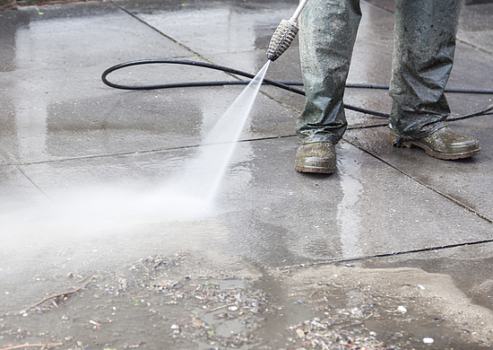 Ein Gebäudereiniger beseitigt Schmutz mit einem Hochdruck-Wasserstrahl. Dabei trägt er wasserdichte Schuhe. 