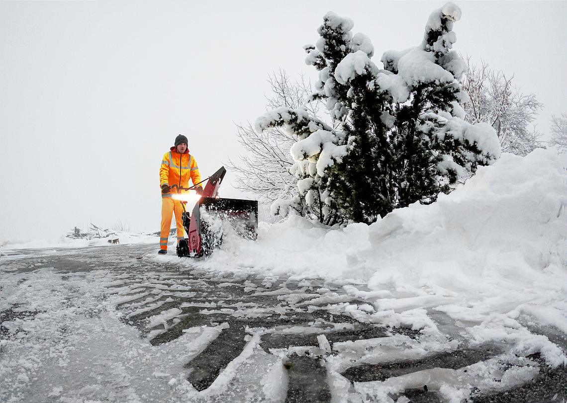 Winterdienstmitarbeiter beseitigt mit einer Fräse Schnee auf einem Weg. 