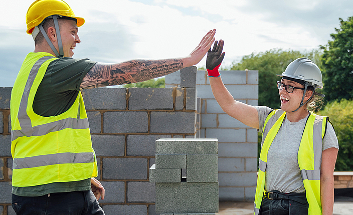 Ein Maurer klatscht mit einer Maurerin ab und feiert den Arbeitserfolg.