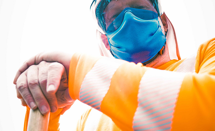 Portraitaufnahme eines Bauarbeiters bekleidet mit UV-Schutzkleidung sowie einem Mund-Nasen-Schutz. 
