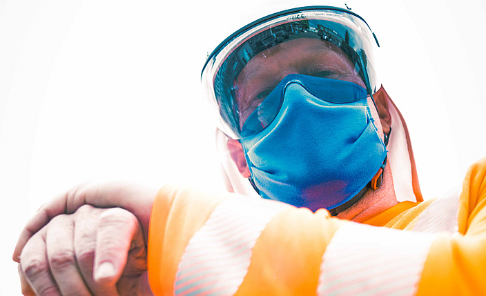 Portraitaufnahme eines Bauarbeiters bekleidet mit UV-Schutzkleidung sowie einem Mund-Nasen-Schutz. 
