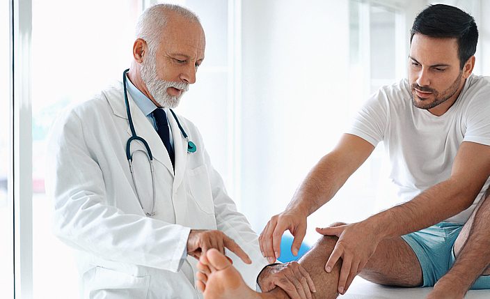 Ein Arzt untersucht einen Knöchel eines Patienten. 