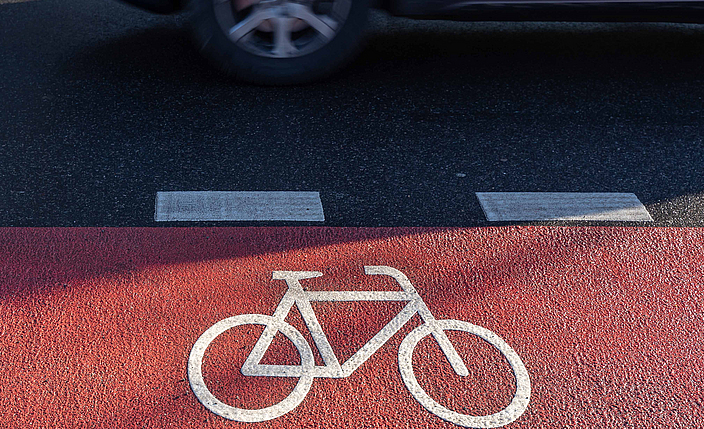Roter Fahrradweg  auf einer Straße. Daneben fährt ein Auto.
